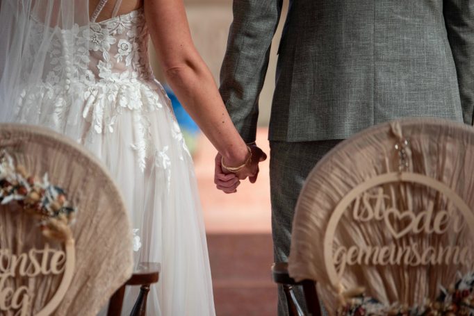Hochzeitsprofil von Paar, das Händchen haltend vor dekorierten Stühlen steht.