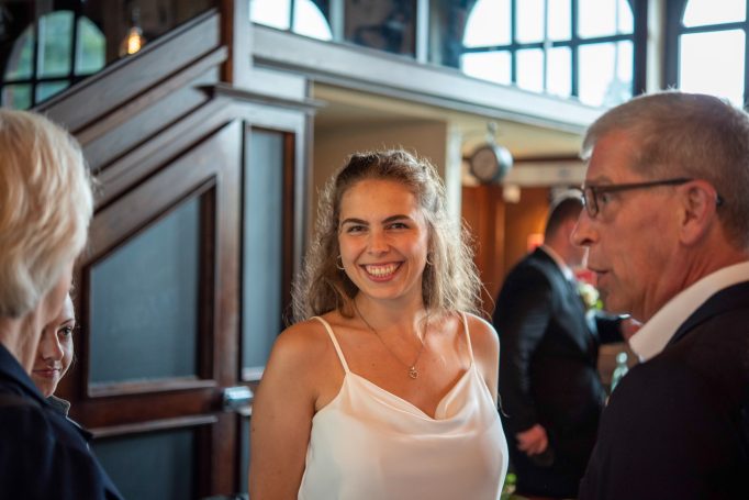 Lächelnde Frau mit lockigem Haar in einem eleganten Raum, umgeben von anderen Personen.